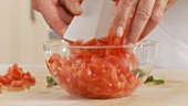 Diced tomatoes being placed in a glass bowl