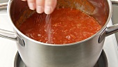 Preparing tomato sauce: adding peeled tomatoes