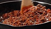Bolognese sauce being stirred in a pan