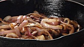 Onion rings being seasoned with pepper whilst in a pan