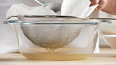 Broth being sieved through a sieve lined with kitchen paper
