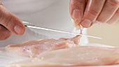 Fat and sinews being cut away from chicken breasts