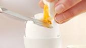 A breakfast egg being cut with a knife and salted