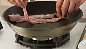Rashers of bacon being placed in a pan