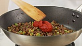 Tomato puree being added and stired into to a minced meat and vegetable mixture