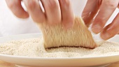 An escalope being dusted in bread crumbs
