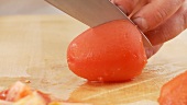 A peeled tomato being quartered