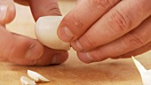 A garlic clove being peeled and the lower end being cut off