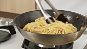 Spaghetti mit gebratenen Speckwürfeln vermischen