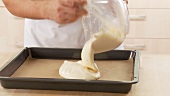 Sponge cake dough being spread in a baking tray lined with grease-proof paper