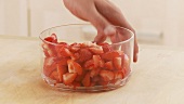A hand taking a bowl of strawberry pieces