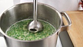 Pea soup being pureed with a hand blender