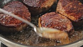 Beef steaks being fried and poured with butter