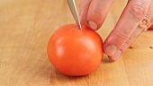 A fresh tomato being slit with a knife