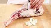 Garlic cloves being inserted into a leg of lamb