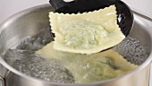 Ravioli being removed from boiling water with a draining spoon