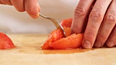 A peeled tomato being deseeded