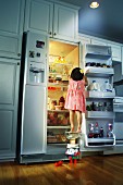 Kleines Mädchen versucht Kuchen im Kühlschrank zu erreichen