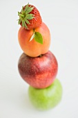 A strawberry, an apricot and two apples stacked on top of each other