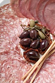 A meat platter with olives, capers and breadsticks