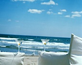 Zwei Martinis auf Armlehnen von weissen Stühlen am Strand