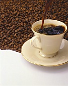 Kaffee wird in Tasse gegossen; Untergrund: Kaffeebohnen