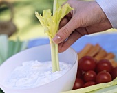 A Hand Dipping a Celery Stick into Dip