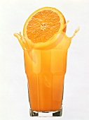 Orange Half Splashing into a Glass of Orange Juice