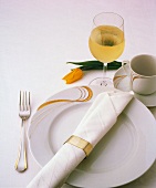 Ein Gedeck mit weisser Serviette, gelber Tulpe und Weißwein