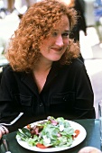 Junge Frau isst Salat im Freien
