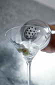 Martini Cocktail aus einem Shaker in ein Glas einschenken