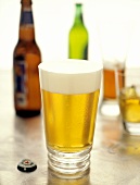 Helles Bier im Glas vor Bierflaschen und Gläsern