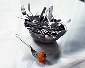 A cherry tomato on fork in front of bowl with cutlery
