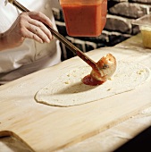 Chef Ladling Sauce on Rolled Pizza Dough