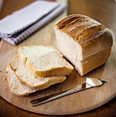 A Partially Sliced Loaf of White Bread on a Wooden Board