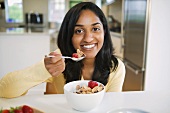 Lachende junge Frau isst Müsli mit Erdbeeren