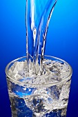 Wasser in Glas mit Eiswürfeln gießen