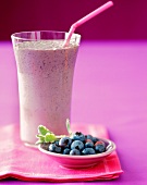 A Blueberry Smoothie in a Glass with a Bowl of Fresh Blueberries
