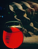 A Glass of Red Wine with Dusty Bottles