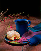 Angebissener Krapfen und blaue Kaffeetasse auf Teller