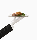 A Gloved Hand Holding a Silver Tray with Steak and Baked Potato
