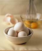 A bowl of eggs, bowl with eggs being beaten behind