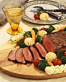 Partially Sliced Steak Cooked Rare on a Cutting Board Surrounded with Vegetables