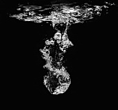 An Ice Cube Dropping into Water Leaving a Trail of Bubbles, Black Background