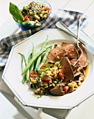 Sliced Lamb with Eggplant and Corn Salsa and Green Beans on a Plate with Fork and Knife