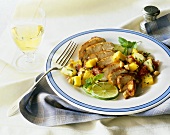 Sliced Roast Pork Loin with Mango Salsa and Lime Slices on a Plate with Fork; Glass of White Wine