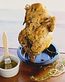 Chicken on a Vertical Roaster; Small Bowl of Herbed Butter with Basting Brush