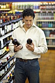 Mann vergleicht zwei Weinflaschen im Supermarkt