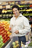 Mann füllt Äpfel in Plastiktüte am Obststand im Supermarkt