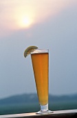 Glass of wheat beer with lemon against sunset